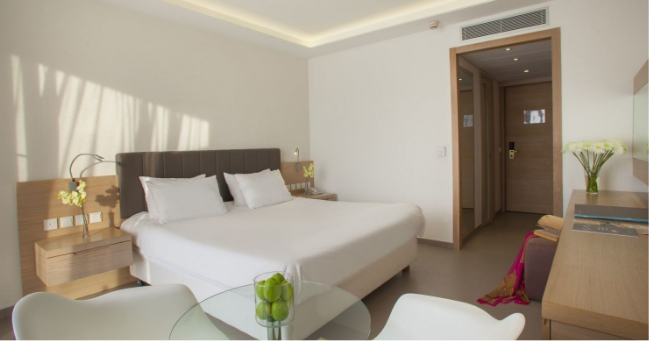 Royal Apollonia Hotel twin bedroom with bed, bedside tables and plant pots.